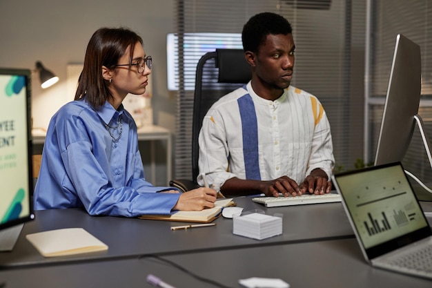 Portrait d'un jeune homme afro-américain utilisant un ordinateur portable tout en collaborant avec une collègue au bureau