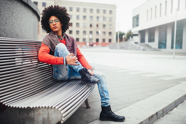 Portrait d'un jeune homme afro assis sur un banc en ville