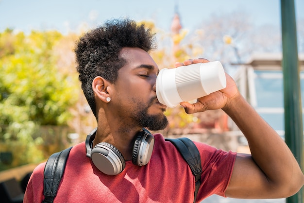 Portrait de jeune homme afro avec un casque et boire une tasse de café à l'extérieur. Concept urbain et lifestyle.