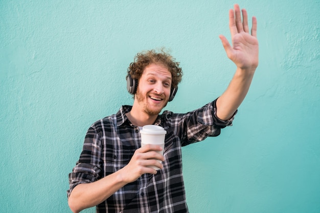 Portrait de jeune homme agitant sa main et sourire en disant bonjour à quelqu'un contre l'espace bleu clair.