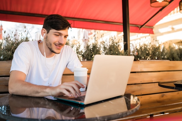 Portrait de jeune homme à l'aide de son ordinateur portable alors qu'il était assis dans un café.