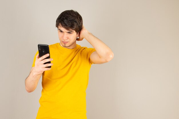 Portrait d'un jeune homme à l'aide d'un téléphone mobile contre le gris.