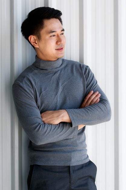 Portrait de jeune homme asiatique beau souriant portant un t-shirt gris à manches longues debout sur un fond en acier inoxydable.