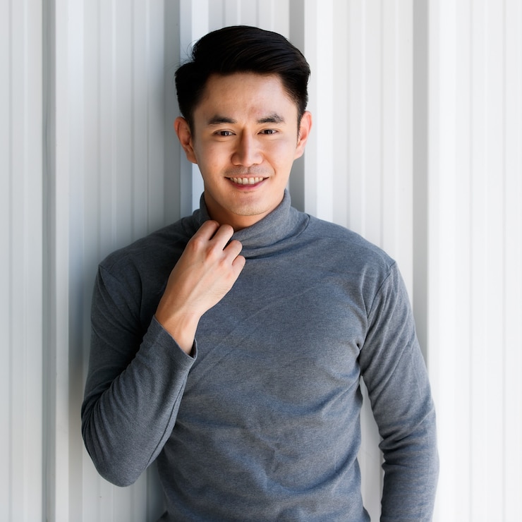 Photo portrait de jeune homme asiatique beau souriant portant un t-shirt gris à manches longues debout sur un fond en acier inoxydable.