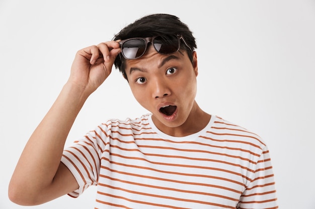 Portrait d'un jeune homme asiatique choqué à lunettes de soleil