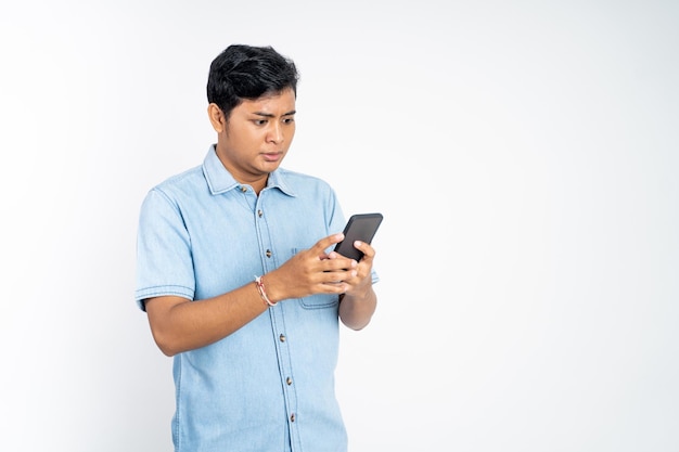 Portrait d'un jeune homme asiatique choqué en regardant une vidéo à l'aide d'un téléphone portable sur fond isolé