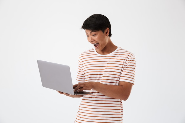 Portrait d'un jeune homme asiatique gai utilisant un ordinateur portable