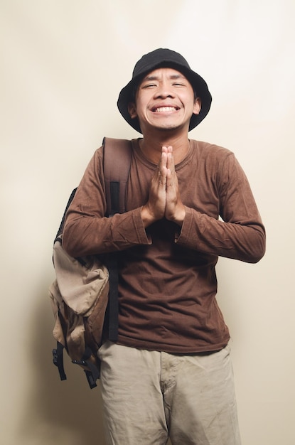 Portrait d'un jeune homme asiatique heureux portant un chapeau noir portant un sac à dos pour voyager isolé sur fond