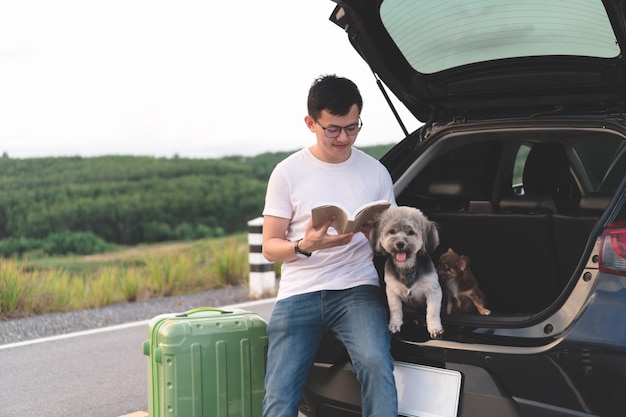 Portrait de jeune homme asiatique lisant un livre assis dans la voiture ouvrir le coffre avec ses chiens.