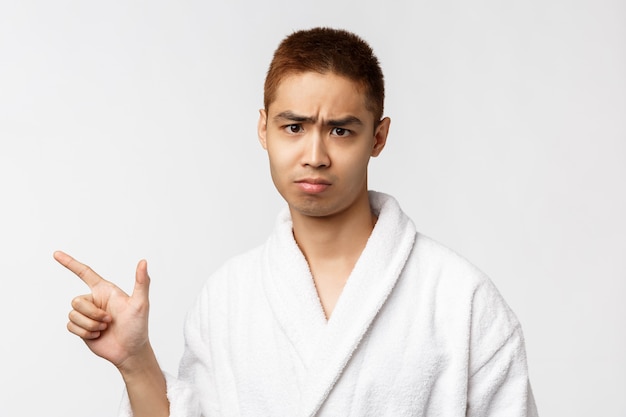 Portrait de jeune homme asiatique en peignoir montrant le geste. Après la douche