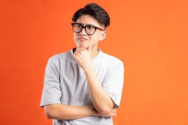 Portrait de jeune homme asiatique pensant, isolé sur fond orange