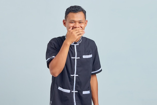 Portrait d'un jeune homme asiatique portant un uniforme de karaté riant d'une blague folle avec les mains sur le corps