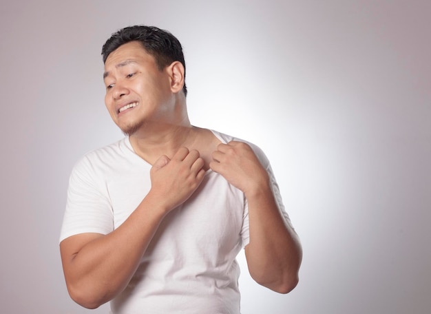 Portrait d'un jeune homme asiatique qui se gratte le corps de douleur.