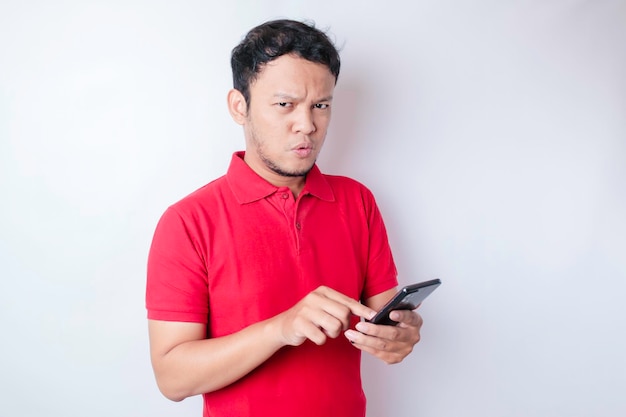 Portrait d'un jeune homme asiatique réfléchi portant un t-shirt rouge regardant de côté tout en tenant un smartphone