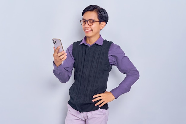 Portrait d'un jeune homme asiatique souriant en chemise décontractée regardant un smartphone lisant des nouvelles en ligne isolé sur fond blanc