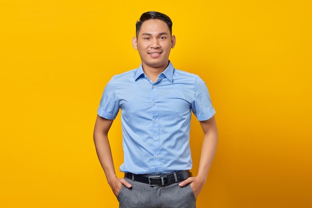 Portrait d'un jeune homme asiatique souriant dans des verres tenant les mains ensemble et se sent optimiste isolé sur fond jaune concept d'homme d'affaires et d'entrepreneur
