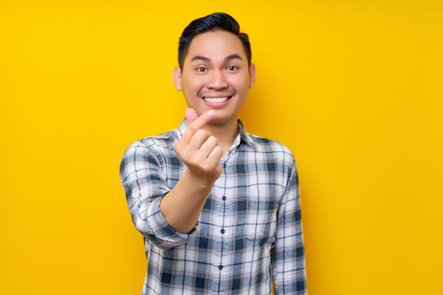 Portrait d'un jeune homme asiatique souriant et sympathique portant une chemise à carreaux montrant un geste de coeur coréen isolé sur fond jaune Concept de style de vie des gens