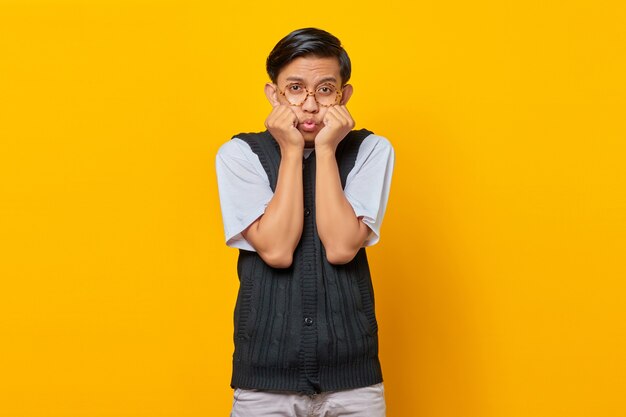 Portrait de jeune homme asiatique surpris avec la main sur le menton sur fond jaune