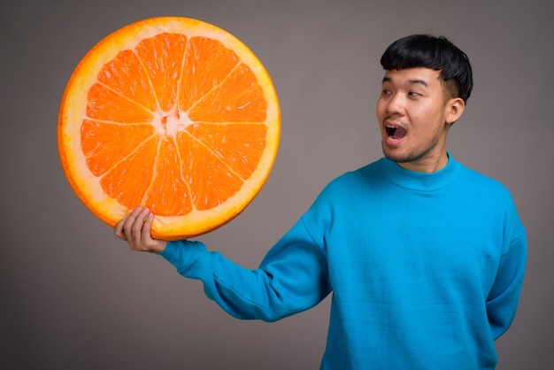 Portrait de jeune homme asiatique tenant une grosse tranche d'orange