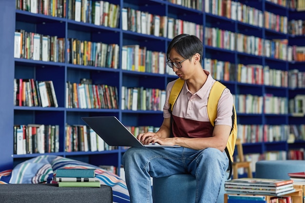 Portrait d'un jeune homme asiatique utilisant un ordinateur portable dans le salon de la bibliothèque avec un espace de copie aux tons bleus vibrants
