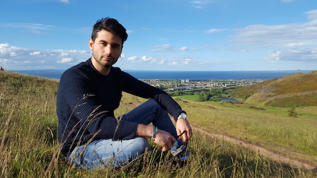 Photo portrait d'un jeune homme assis sur un champ contre le ciel