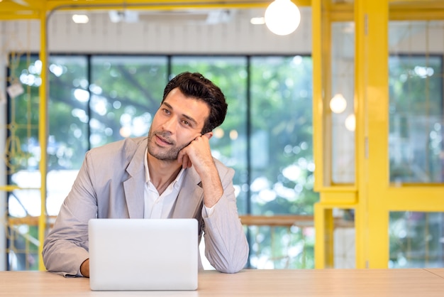 Portrait de jeune homme assis à son bureau dans le bureau moderne, homme d'affaires concentré travaillant sur un ordinateur portable pensant