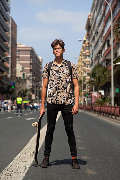 Portrait d'un jeune homme authentique avec planche à roulettes au milieu de la rue.
