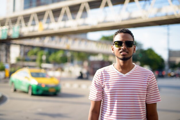 Portrait de jeune homme barbu africain beau avec des cheveux afro contre vue sur la passerelle dans les rues de la ville à l'extérieur