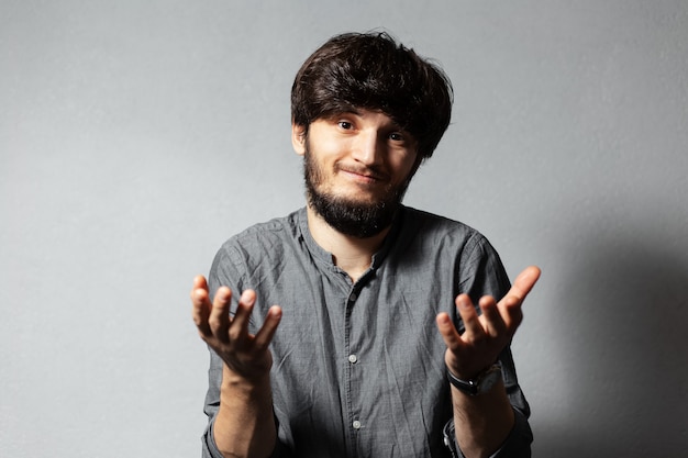 Portrait de jeune homme barbu aux cheveux ébouriffés, montrant un geste impuissant avec les mains