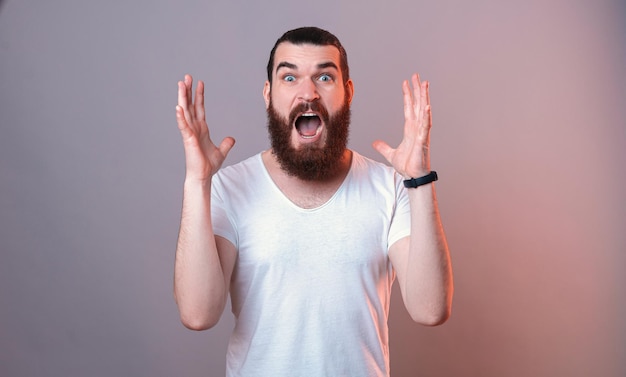 Portrait d'un jeune homme barbu choqué portant un T-shirt blanc se tenant la main près du visage Sudio photo avec lumière rouge