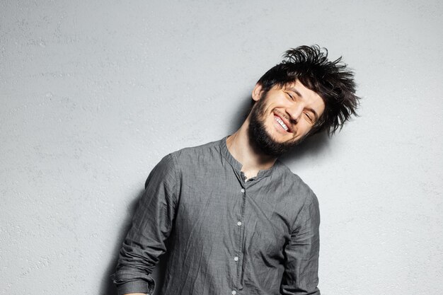 Portrait de jeune homme barbu heureux aux cheveux ébouriffés sur fond gris.