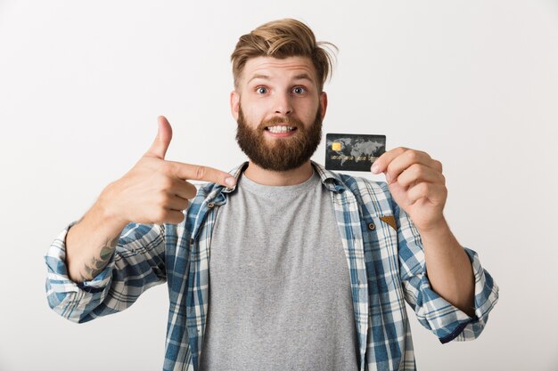 Portrait d'un jeune homme barbu heureux montrant la carte de crédit isolé sur fond blanc