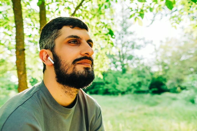 Portrait de jeune homme barbu de race blanche avec des écouteurs à l'extérieur avec fond de végétation