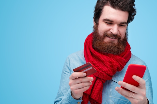 Portrait de jeune homme barbu tenant une carte de crédit et un téléphone mobile