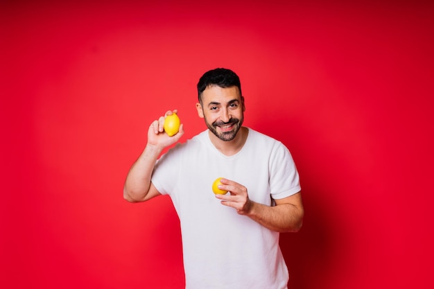 Portrait de jeune homme barbu tenant des citrons dans les deux mains sur fond rouge isolé