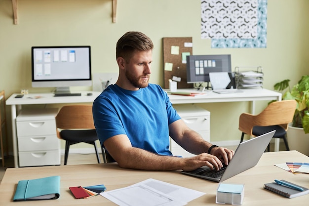 Portrait de jeune homme barbu utilisant un ordinateur portable tout en travaillant au bureau dans un espace de copie de cadre de bureau confortable