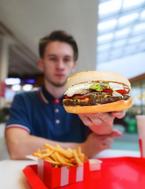 Portrait d'un jeune homme beau et heureux, un mec affamé est assis sur une aire de restauration dans un centre commercial en train de manger