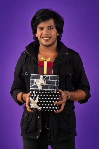 Portrait de jeune homme beau souriant heureux tenant une boîte-cadeau sur fond violet