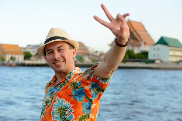 Portrait de jeune homme beau touriste au quai contre vue sur la rivière dans la ville de Bangkok