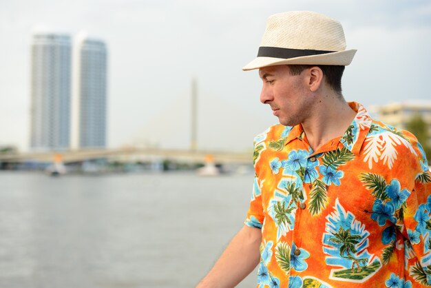 Portrait de jeune homme beau touriste au quai contre vue sur la rivière dans la ville de Bangkok