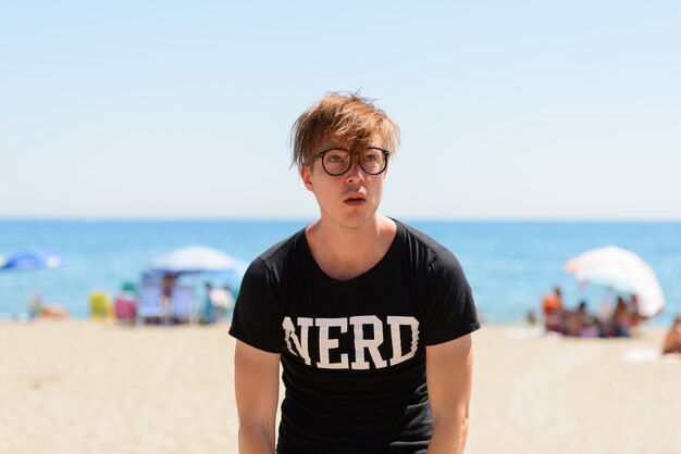 Portrait de jeune homme beau touriste comme nerd à la plage en Espagne