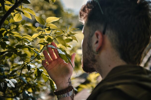 Portrait d'un jeune homme blond sentant des feuilles vertes dans un parc en été