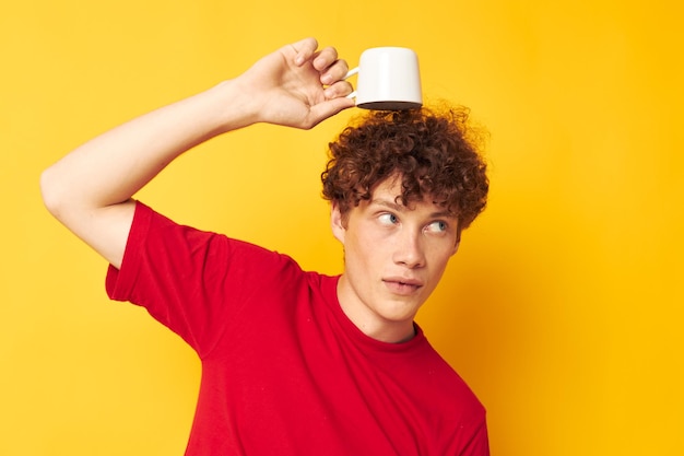 Portrait d'un jeune homme bouclé posant avec une tasse blanche et dans les mains d'une boisson fond jaune inaltéré