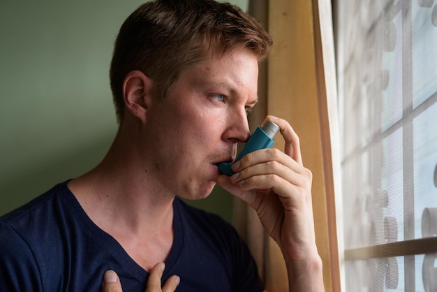 Photo portrait d'un jeune homme buvant par la fenêtre de sa maison