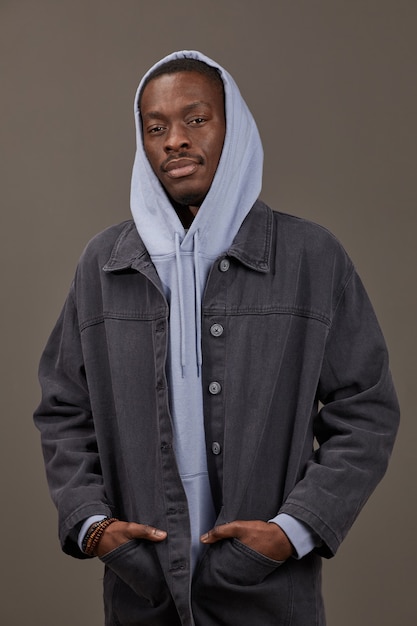 Portrait de jeune homme à capuche et en veste de jeans posant à l'avant isolé sur mur gris