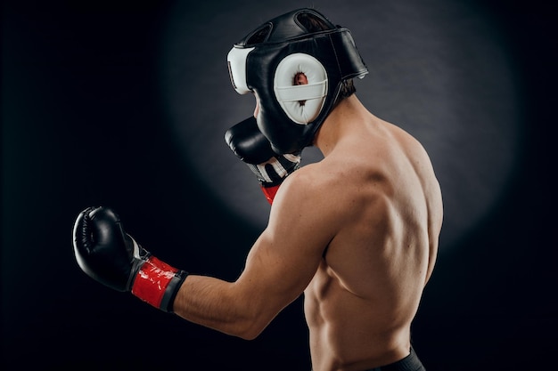 Portrait d'un jeune homme avec un casque de boxe et des gants sur fond sombre