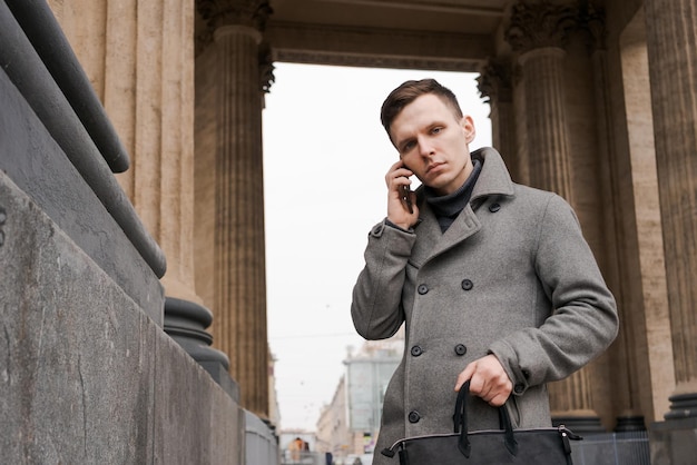 Portrait jeune homme caucasien à l'aide de son téléphone portable dans des porte-manteaux gris