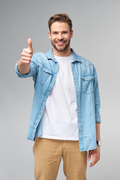 Portrait de jeune homme caucasien beau en chemise de jeans montrant grand pouce vers le haut de geste debout