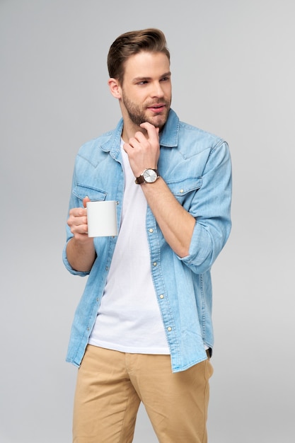 Portrait de jeune homme caucasien beau en chemise de jeans tenant une tasse de café