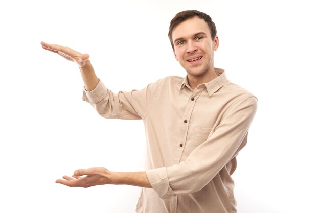 Portrait d'un jeune homme caucasien brun drôle montrant la taille avec les mains ou tenant quelque chose d'isolé sur fond de studio blanc